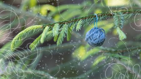 Christmas background with balls of yarn. Blue wool ball hanging on the green branches of a Christmas tree. Horizontal poster with copy space. The concept of a winter gift, present for handworkの写真素材