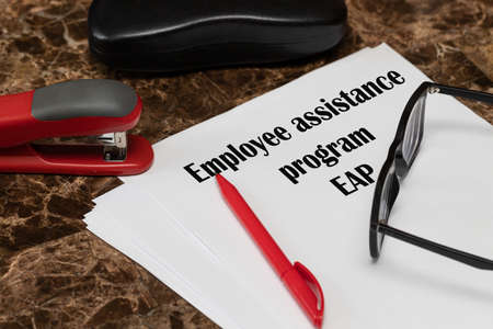 EAP employee assistance program. The text is written on white paper, next to a red pen, a hole punch...