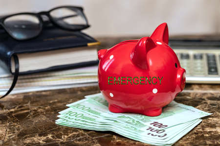 Emergency fund concept. The inscription on the piggy bank, which stands on the banknotes on the marble table, next to it are glasses, a calculator, a diary.の写真素材