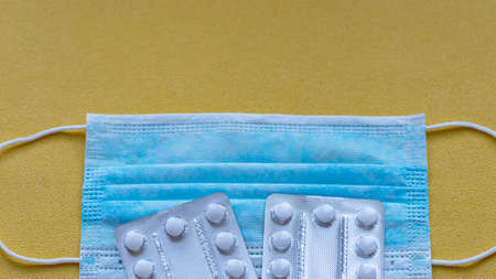 Medical mask and pills on a yellow background. Procedural mask for bacteria. The concept of protection from virus, flu, disease.の写真素材