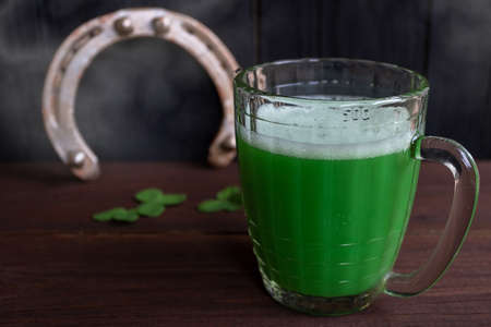 Green Shamrocks clovers on wooden table with a large mug of beer and a gold horseshoe. Background for St. Patrick's day celebrationの写真素材