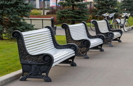 Perspective of empty white benches in a row at public park alley