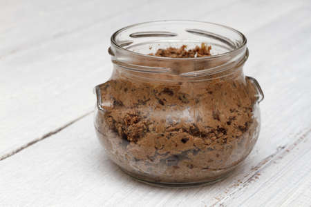 Chicken liver pate with prunes and apple in a glass jar on a white wooden background. A simple...