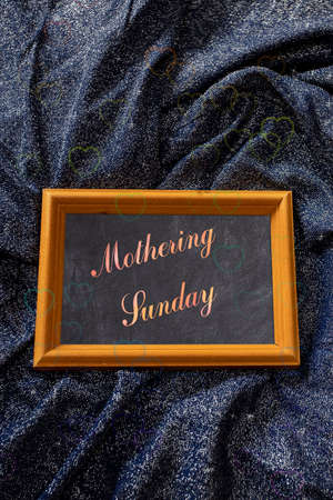 Mother's Day composition. Text Mothering Sunday on a chalk board lying on a shiny lurex fabric. Congratulations for relatives, friends, colleaguesの写真素材