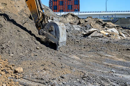 Bucket of an earthmover digging a pile of sand on the background of new houses under construction at demolition construction siteの写真素材