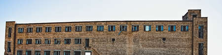 Abandoned multi-story red brick factory building with broken glass windows. A toned image