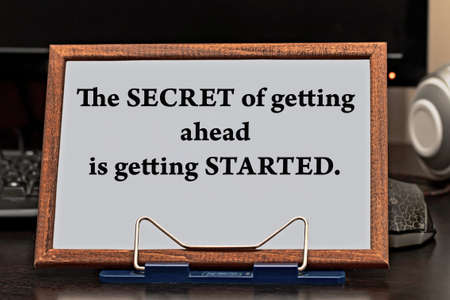 Motivational quote inspiring success. The secret to getting ahead is getting started written in a wooden frame against the background of the computer on the desktop.の写真素材