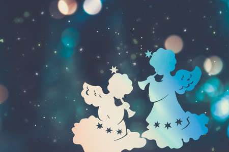 Silhouettes of two christmas angels on a multicolored bokeh background against the night blue skyの写真素材