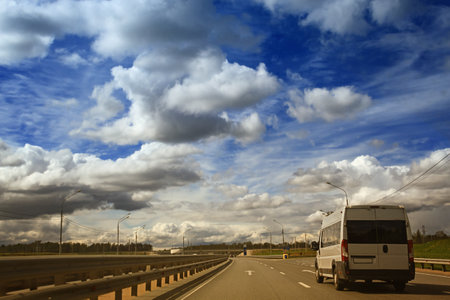 White modern passenger charter van with a small delivery moves fast on the highway to the urban suburbs. Business distribution and logistics express service. Mini bus rides along the highwayの写真素材