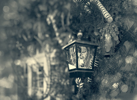 Red lantern with a snowman on it is hanging on a Christmas tree. The lantern is surrounded by green leaves and red berries. The scene is festive and cheerfulの写真素材