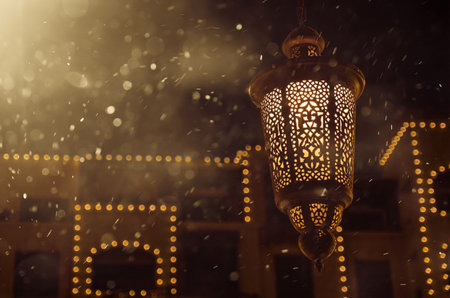 Ornamental Arabic lantern glowing at night and glittering golden bokeh lights. Festive greeting...