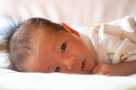 adorable cute newborn baby infant with big black eyes lying on the bed