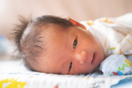 adorable cute newborn baby infant with big black eyes lying on the bedの写真素材