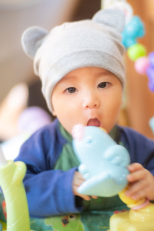 focus in the eyes ofAsian infant baby wearing beanie hat and playing toy by bring it to the mouthの写真素材