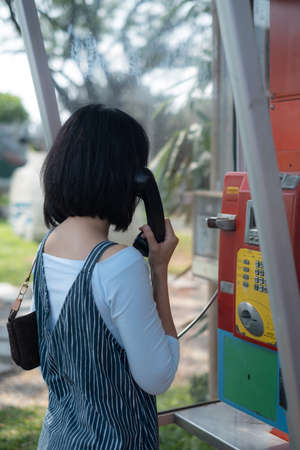 Woman using oldstyle plublic pay phone in telephone booth.の写真素材