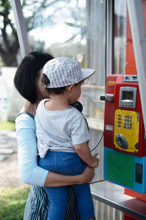 Woman and child Mother and Kid Boy Baby using oldstyle plublic pay phone in telephone boothの写真素材