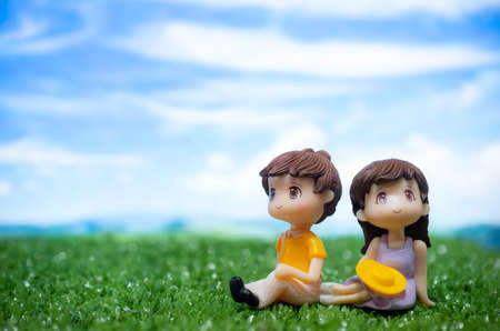 Miniature doll couple boy and girl sitting on the field with a blank direction sign and blue sky backgroundの写真素材
