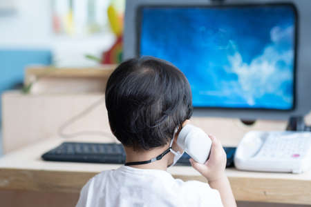 Asian Baby boy with black hair talking to telephone in front of computer laptop notebookの写真素材