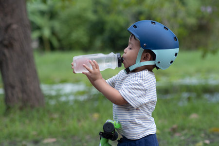 Cute Baby boy on a bike wearing helmet drinks water from water bottleの写真素材