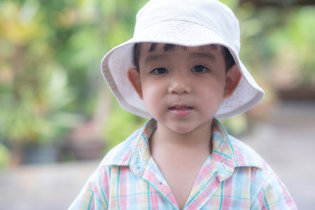 close up portrait of beautiful sweet boy, wearing White bucket hat and colorful shirt, looking at camera, big dark eyesの写真素材