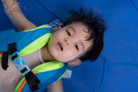 Happy Funny Baby Boy Kid Toddler wearing life jacket playing water in the Swimming poolの写真素材