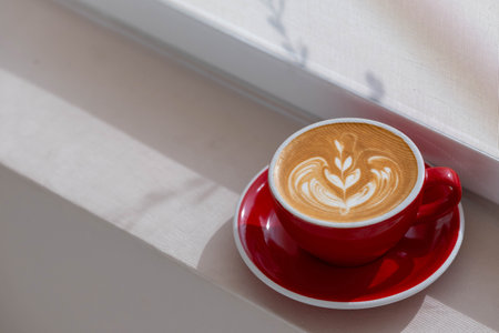 A Red Cup of Coffee Latte with latte art with mornning light through curtainの写真素材
