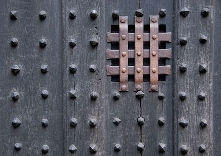 Close-up shot of a dark, ancient, heavy, wooden door with metal spikes and bars over a tiny square window.の写真素材