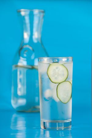 Glass of ice water with sliced cucumbers and a carafe on teal blueの写真素材