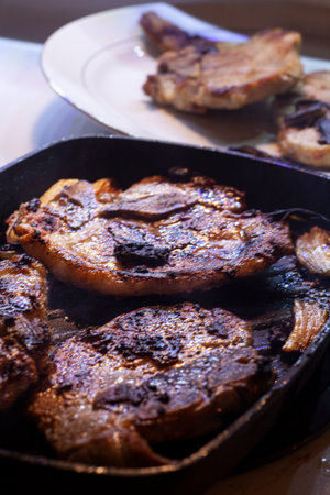 Pork chops grilling in skillet.