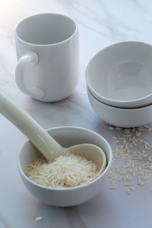 High key white rice in bowl with cup and spoon.