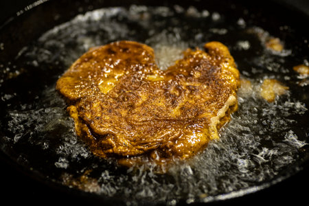 Battered pork chop frying in cast iron skillet.