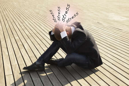 young man sitting on wooden floor with headache and lot of stressの写真素材
