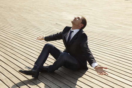 young man sitting on wooden floor with open armsの写真素材