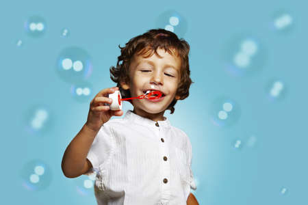 little caucasian boy with soap bubbles on blue backgroundの写真素材
