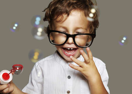 little caucasian boy with soap bubbles on grey backgroundの写真素材