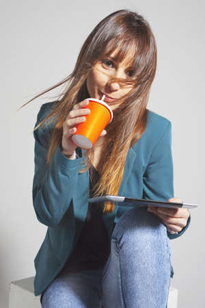 Beautiful business woman with a digital tablet and a refreshment  On a grey backgroundの写真素材