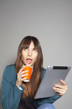 Beautiful business woman with a digital tablet and a refreshment  On a grey backgroundの写真素材