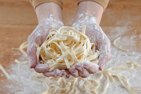 Hands doing fresh italian pasta in wooden backgroundの写真素材