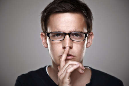 Portrait of a normal man with finger on lips keeping a secretの写真素材