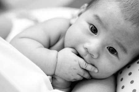 Hungry Asian baby sucking his fingers instead of mother breastfeedingの写真素材