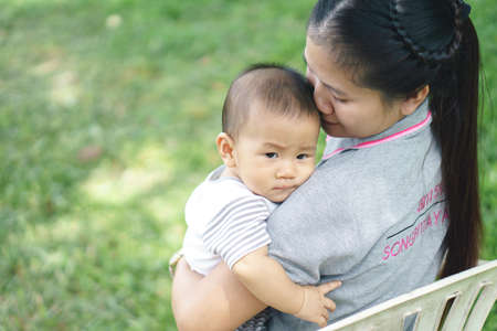 Asian mother holding her son while on duty, Songpittayakom public school was written in her back