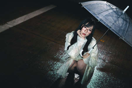 Charming Asian girl  with umbrella and raincoat at nightの写真素材