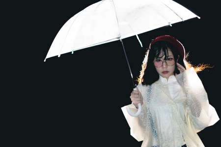 Charming Asian girl  with umbrella and raincoat at nightの写真素材