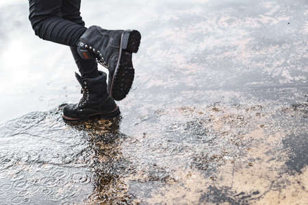 Girl wearing jeans and black combat boots splashing in a puddle after rainの写真素材