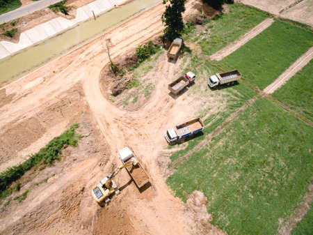 Aerial shot of excavator machine loads a dump truck on harvest field