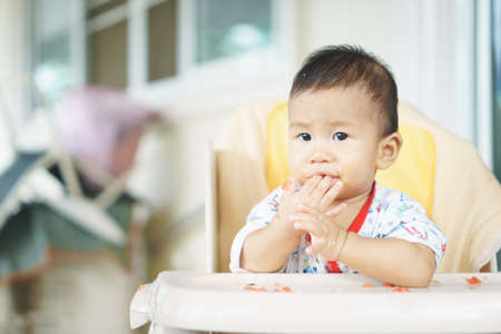 8 months old Asian baby eating food by himselfの写真素材