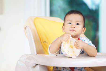 8 months old Asian baby eating food by himselfの写真素材