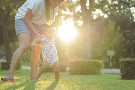 Mother helping Asian baby to learn first step on a lawn in summer dayの写真素材