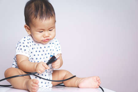 9 months Asian baby curious looking at electronic plugの写真素材