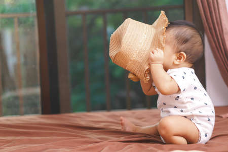 9 months Asian baby playing with hat on the bedの写真素材